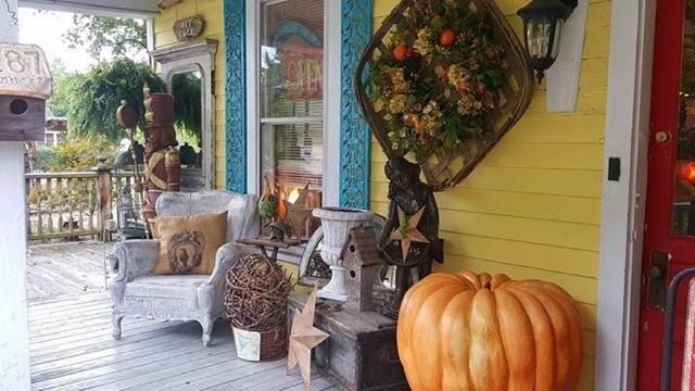 Cozy porch with yellow siding, fall wreath, pumpkin, and wicker chairs on a wooden deck.