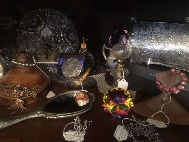 Assorted jeweled handbags and accessories displayed on a dark surface with a silver clutch and ornate mirror.