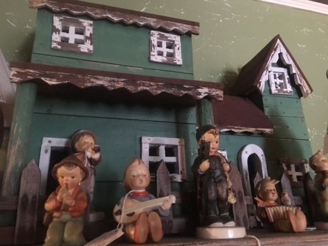 Miniature green house with small figurines standing in front of it, including a child holding a guitar.