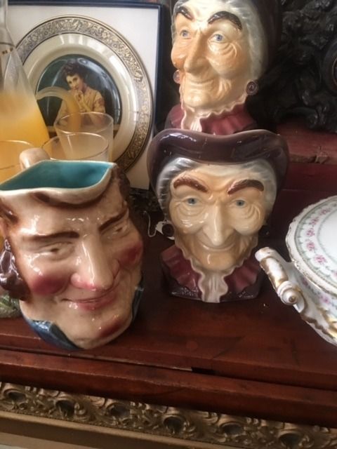 Three ceramic character mugs on a wooden shelf, with a framed picture and plate behind them.