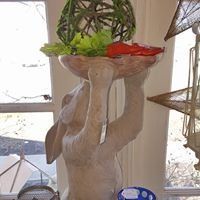 Sculpture of a ceramic rabbit holding a tray of green and red peppers indoors by a window