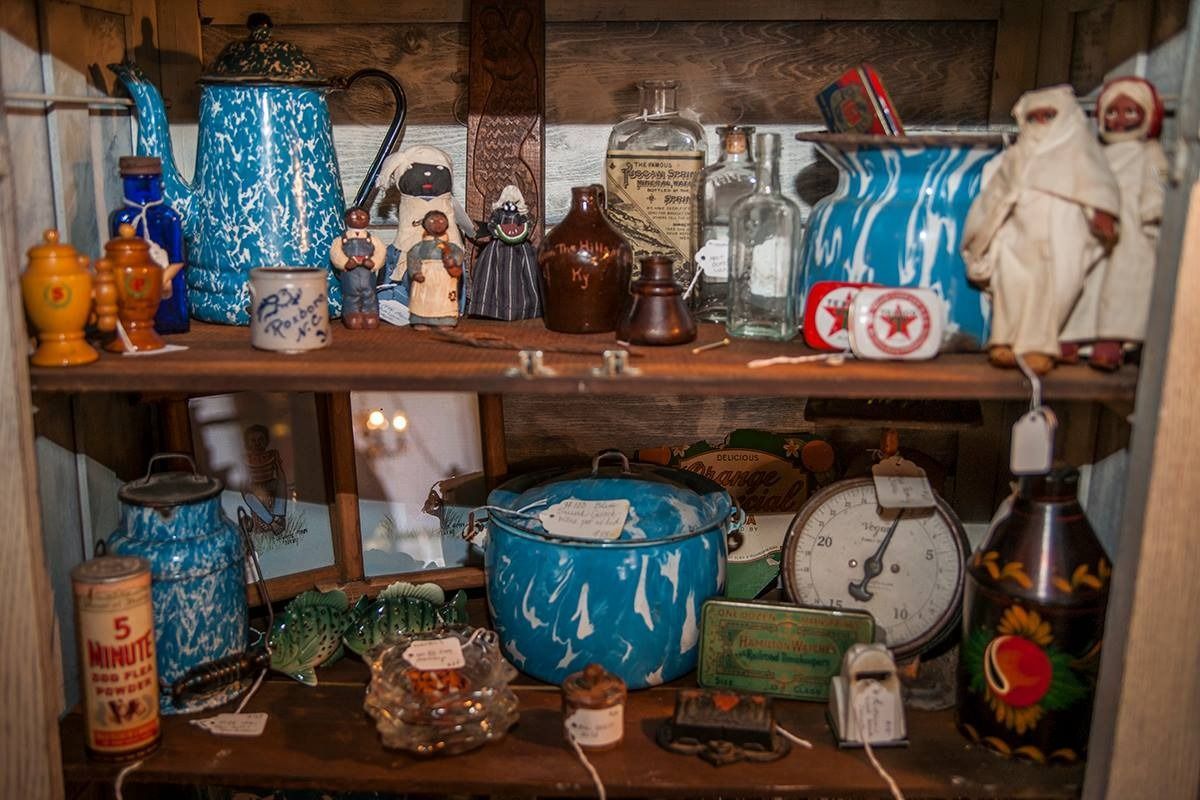 Shelf of assorted vintage jars, tins, and kitchenware in blue, brown, and white on a cluttered table.