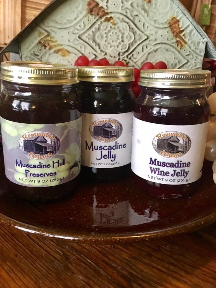 Three jars of dark grape preserves and jelly on a wooden table, with decorative backsplash behind them