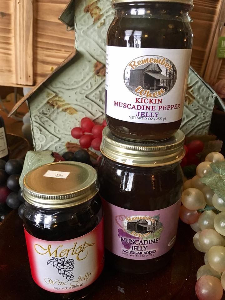 Jars of homemade pepper jellies and preserves stacked on a wooden shelf with grapes and red berries