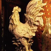 Decorative rooster sculpture with a weathered white finish beside a glass bottle on a warm-toned shelf