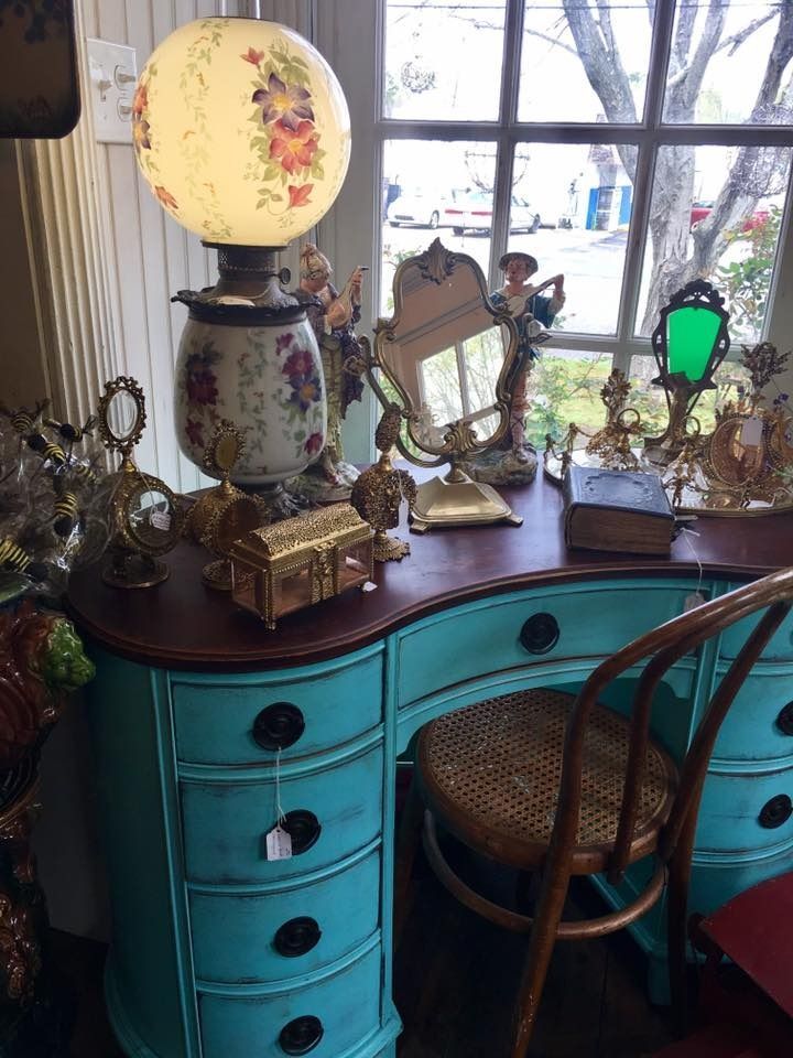 Turquoise vanity with antique lamps and decor beside a window, with a woven chair in front