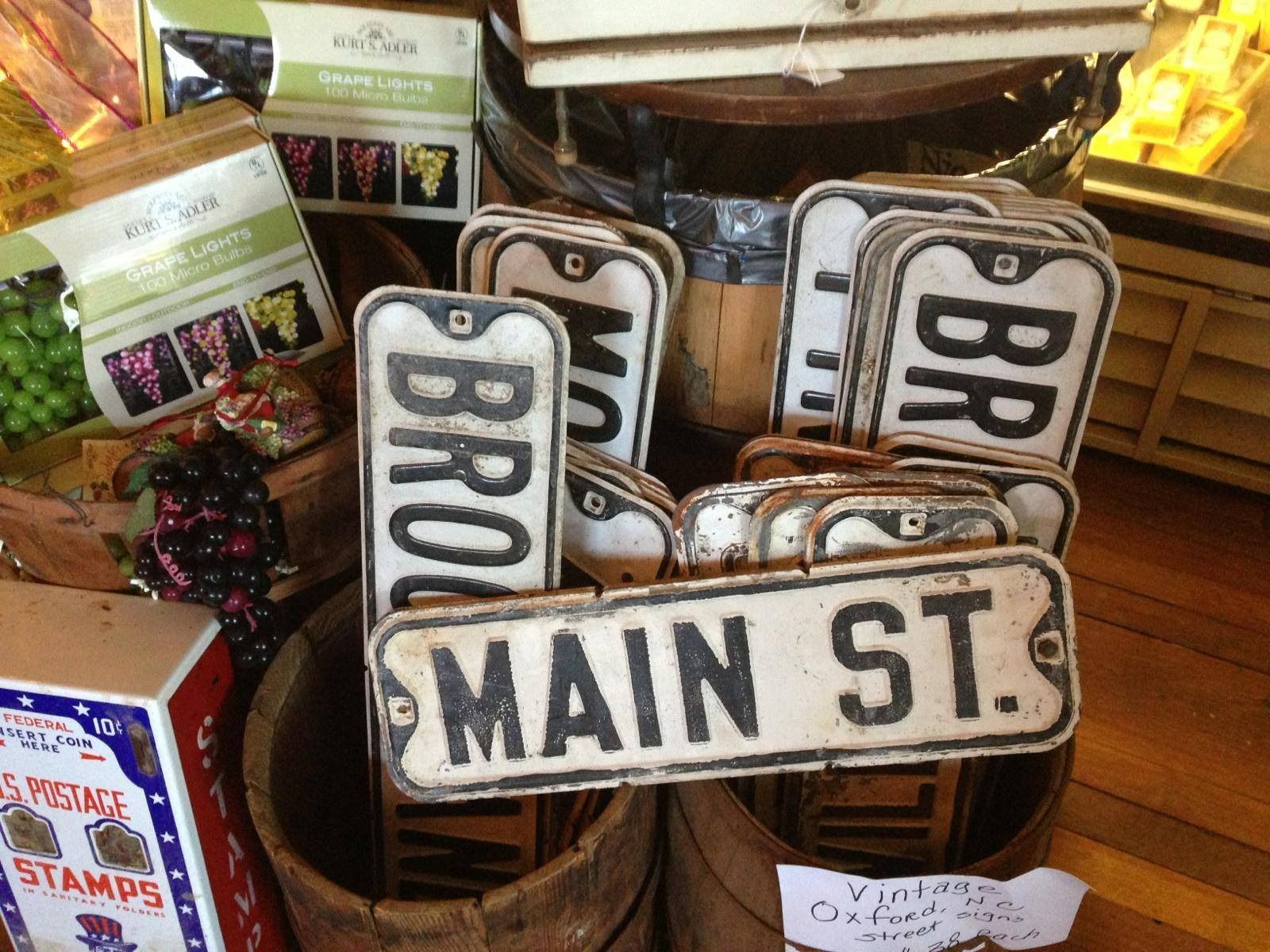 Vintage street signs with MAIN ST., BROAD, and BR on display in a shop basket