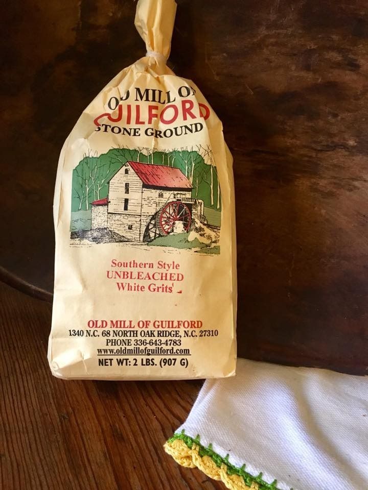 Bag of Old Mill of Guilford stone ground flour on a wooden table beside a white cloth.
