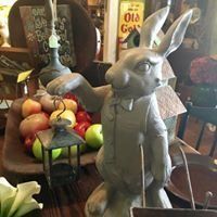 Gray rabbit statue holding a lantern in a cozy market display with apples and pears