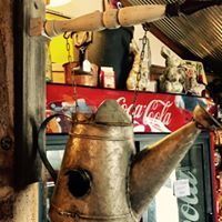 Rustic metal teapot sculpture in a cluttered vintage shop, with a red Coca-Cola sign behind it