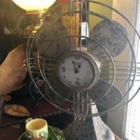 Vintage metal fan with a round clock in the center, beside a lamp and mug indoors