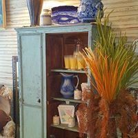 Blue cabinet with shelves of decorative vases and flowers in a rustic room