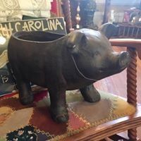 Black pig figurine on a patterned chair, with a South Carolina sign in the background