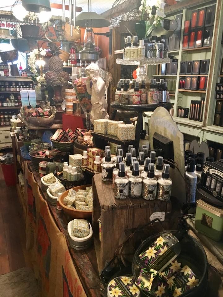 Cluttered gift shop aisle with candles, soaps, jars, and hanging decor on wooden shelves.