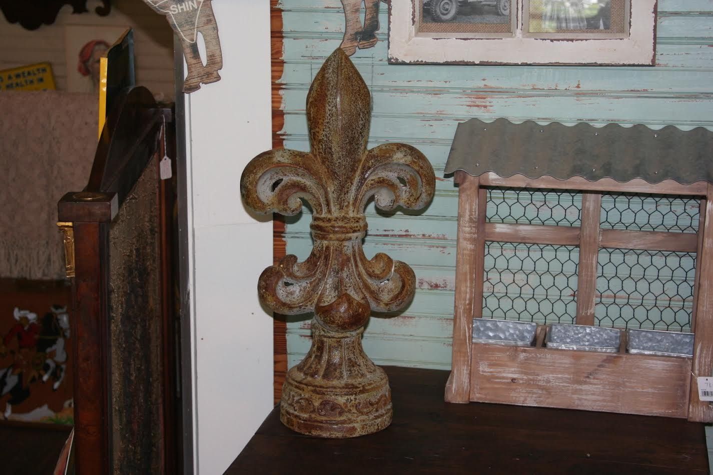 Decorative fleur-de-lis ornament and a small framed window on a shelf against a pale blue wall.