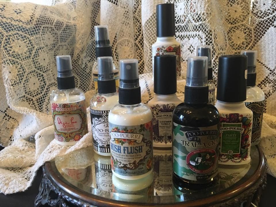 Assorted vintage-style perfume bottles on a mirrored tray in front of lace curtains.