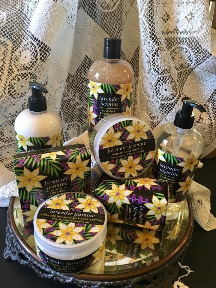 Floral-labeled bath and body products arranged on a tray against a lace curtain backdrop