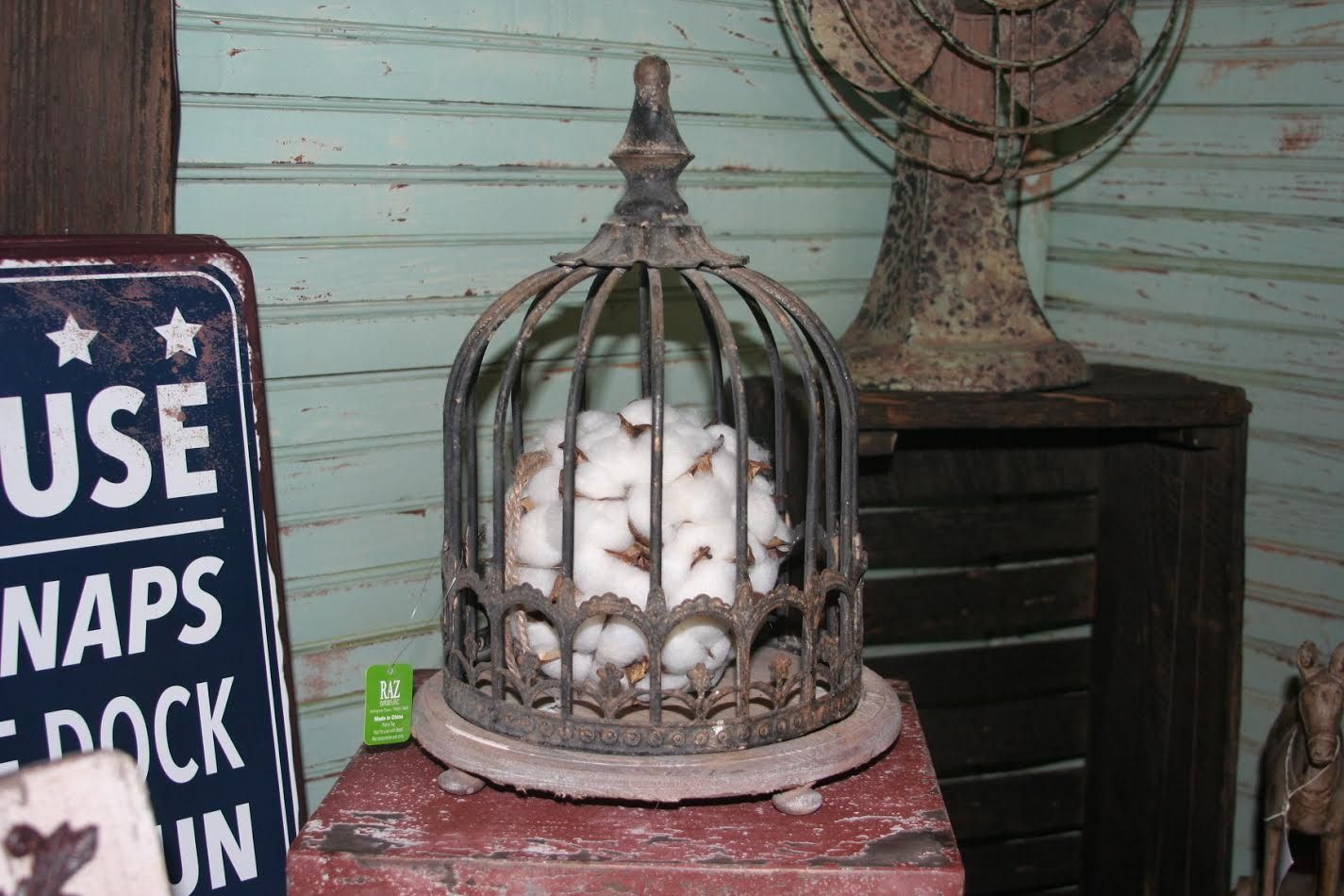 Decorative birdcage filled with white cotton on a red box beside a rustic sign and fan.