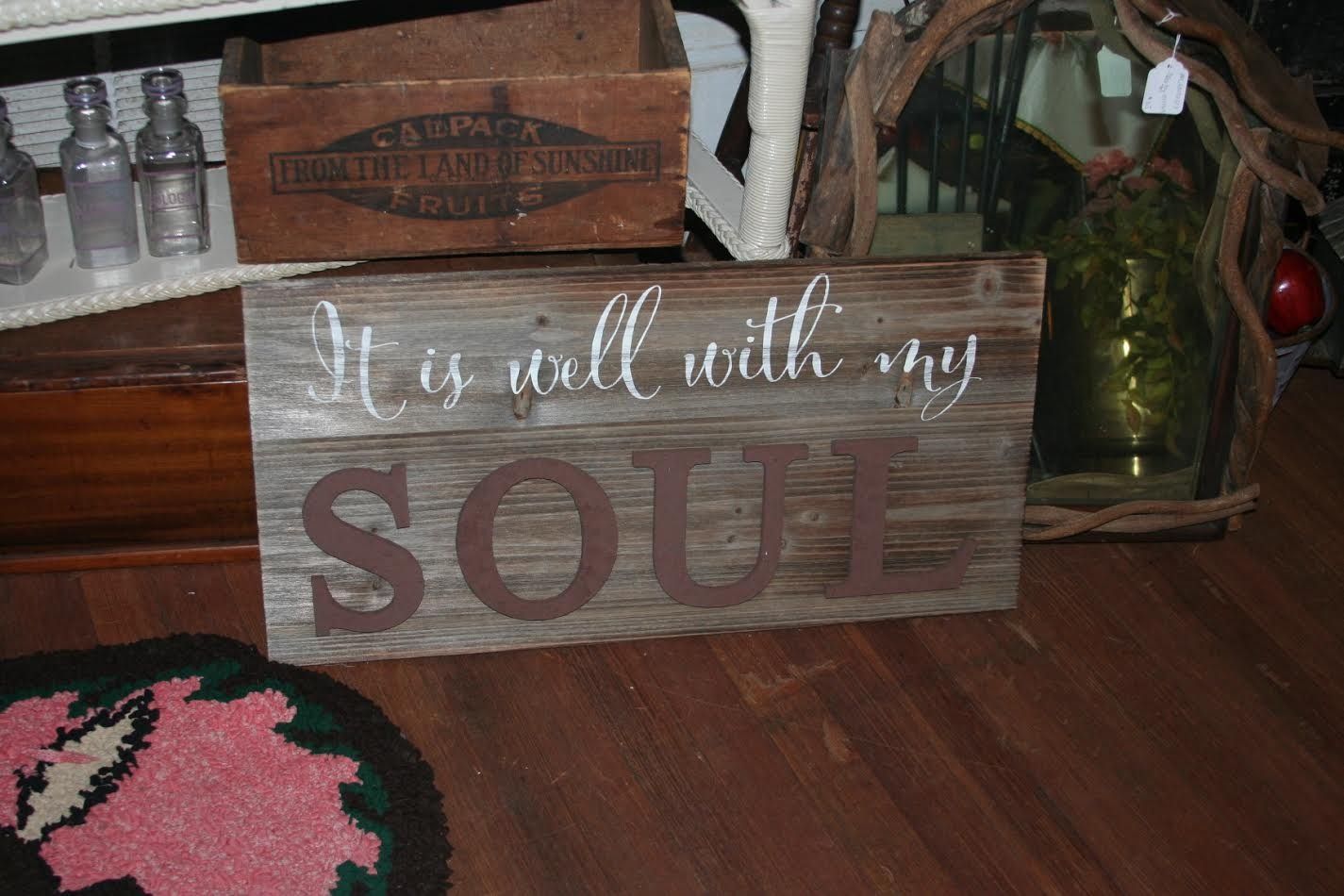 Wooden sign reading “It is well with my SOUL” on a wooden floor near decor.