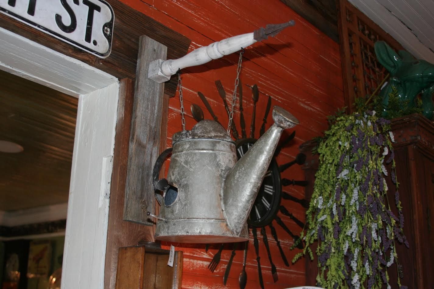 Decorative metal watering can and hanging herbs on a red wooden wall with a wagon wheel