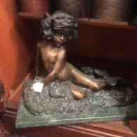 Small bronze child figurine seated on a textured base on a wooden shelf