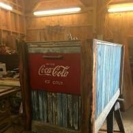 Rustic wooden Coca-Cola booth with red sign and blue slatted sides inside a workshop