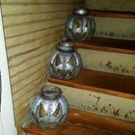Three silver pumpkin lanterns arranged on wooden stairs beside a beige wall.