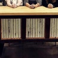 Hands folded on a wooden table with striped cabinet panels beneath it
