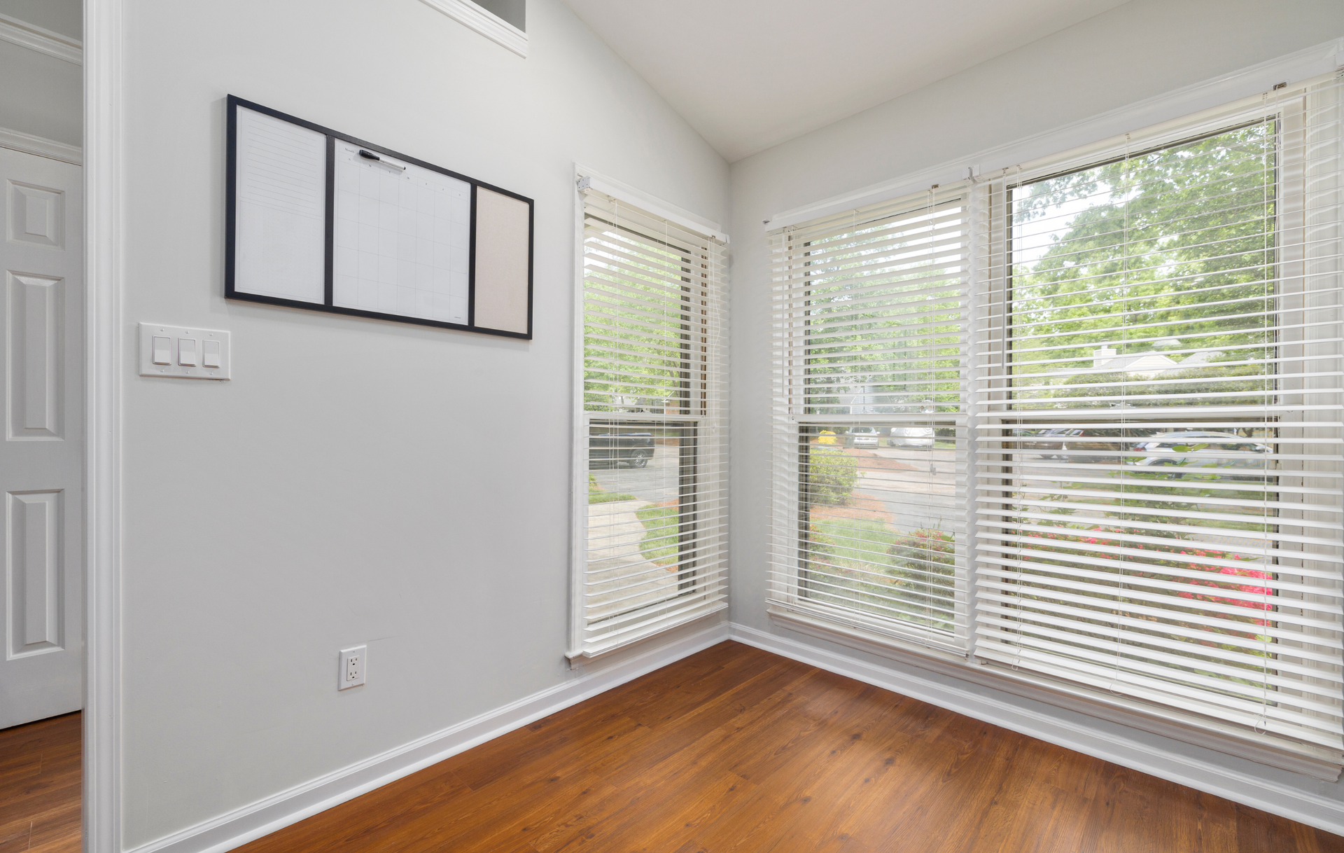 An empty room with hardwood floors and white blinds.