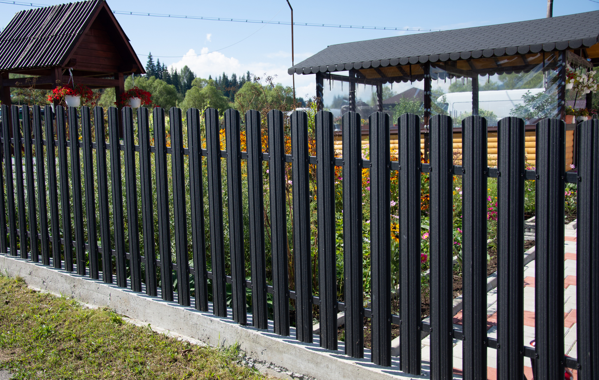 A black metal fence surrounds a lush green yard with a house in the background.