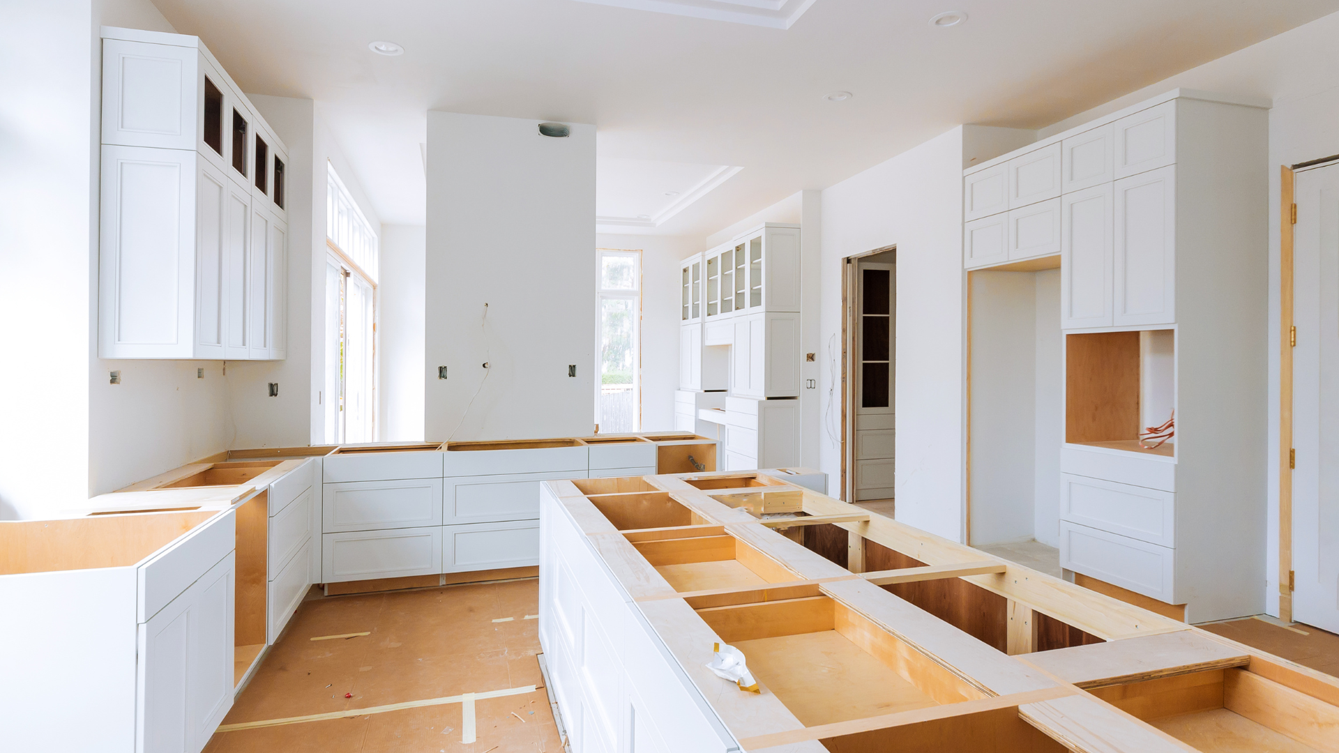 A kitchen under construction with white cabinets and wooden counter tops.