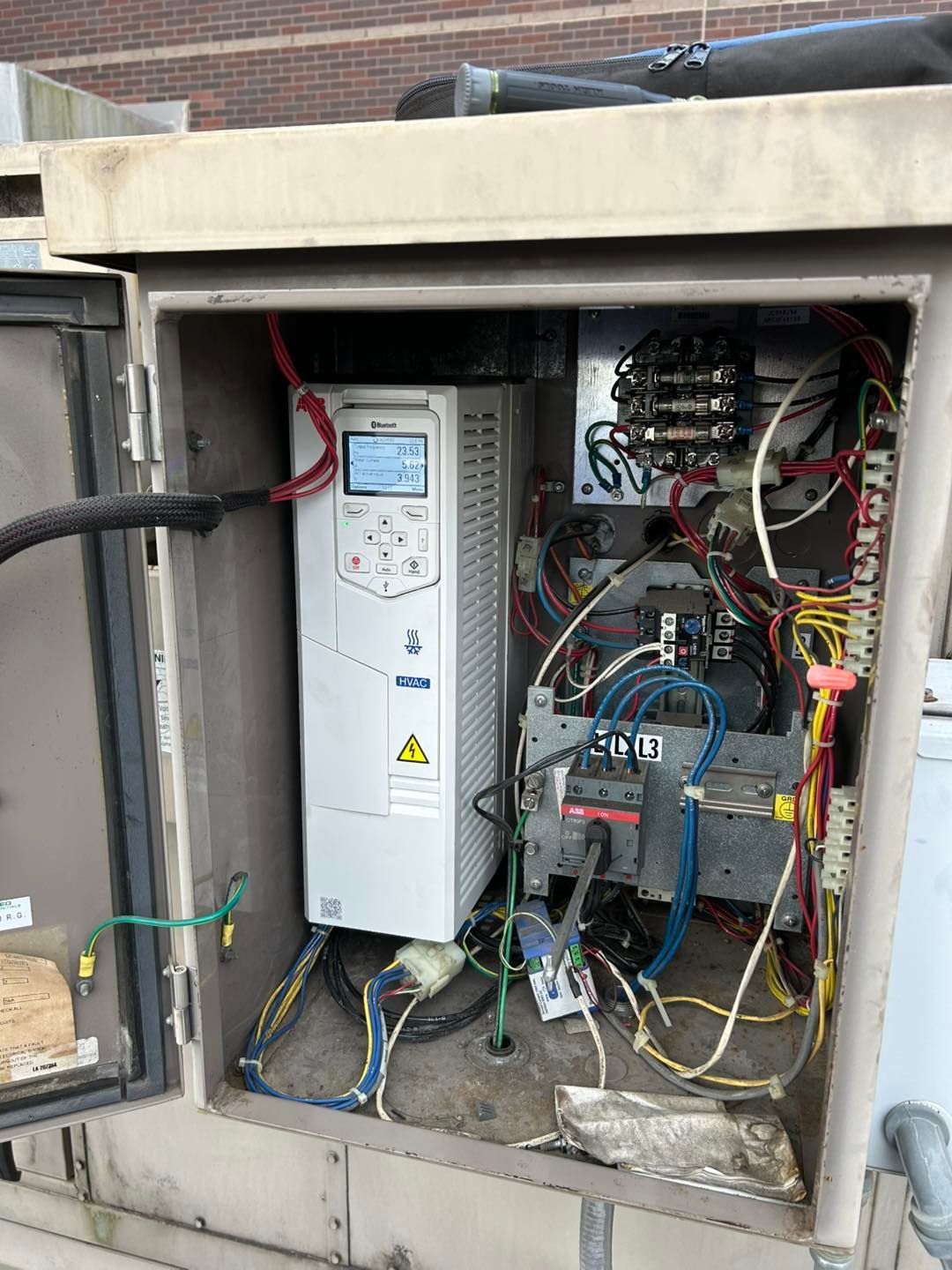 An open, metal electrical box with a drive controller and wiring inside, on a rooftop.