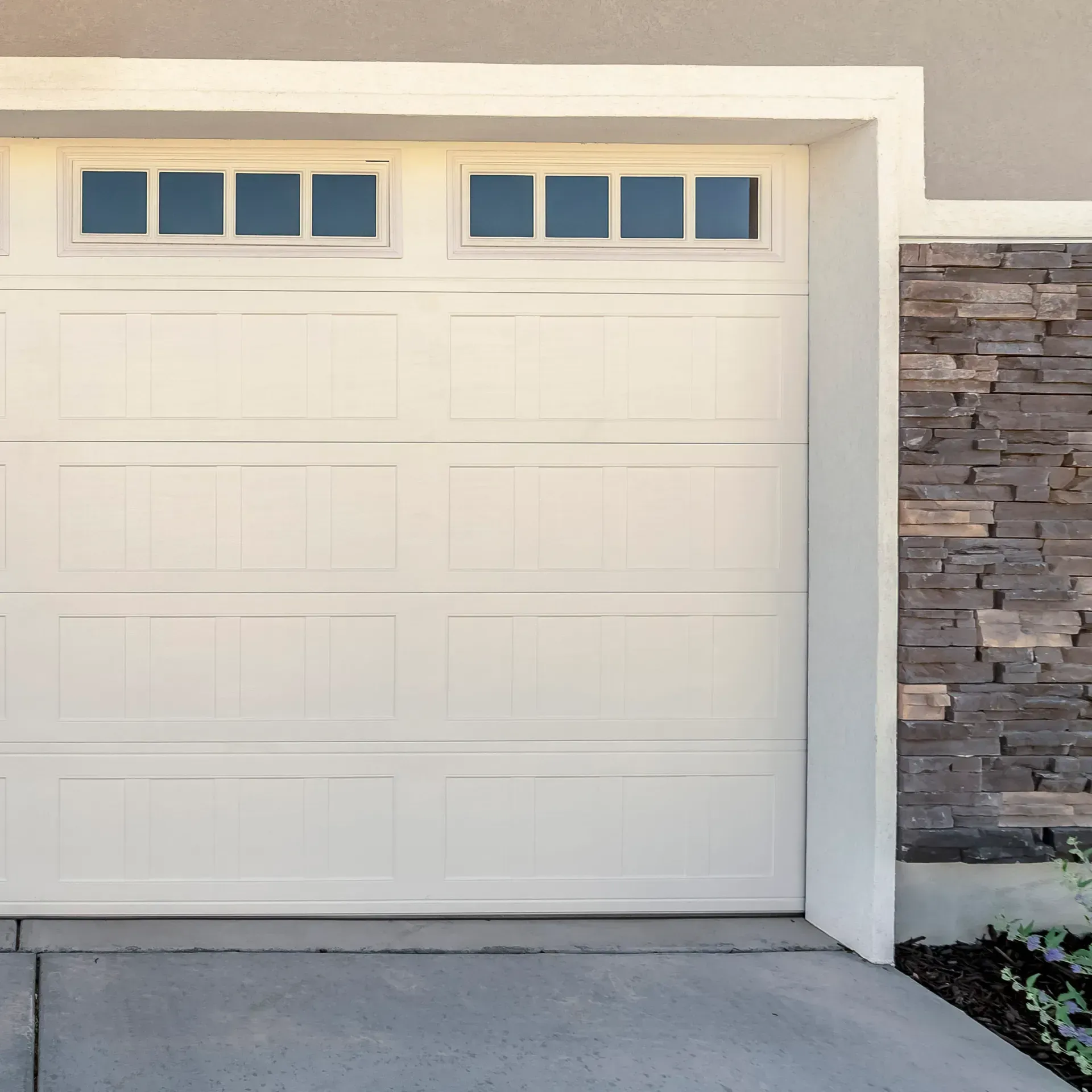 A white garage door with rectangular windows on a house with stone-textured siding.
