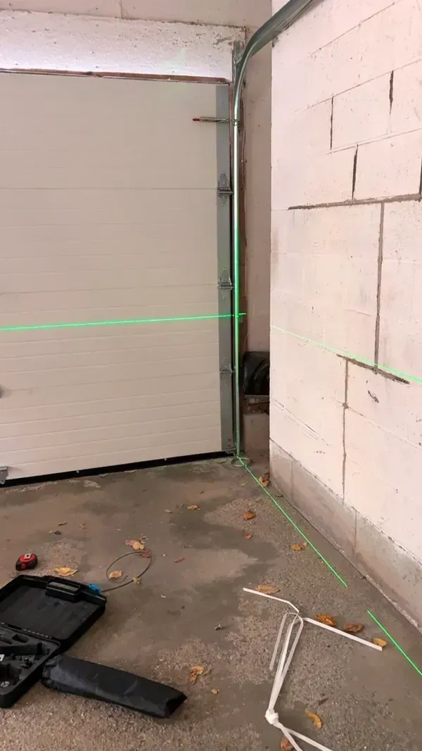 A garage interior showing a green laser level line projected across the wall and floor near a closed garage door.