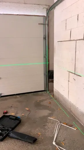 A green laser level line projects across a garage door and a white concrete block wall, creating a precise horizontal.