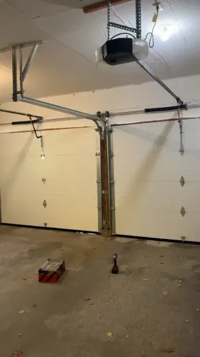 Two white garage doors with a ceiling-mounted opener mechanism in a concrete-floor garage.