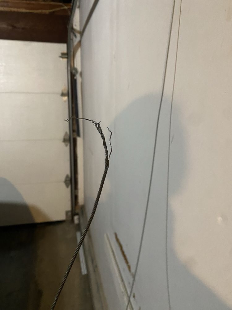 A frayed, broken metal wire hanging in a garage, with the garage door in the background.