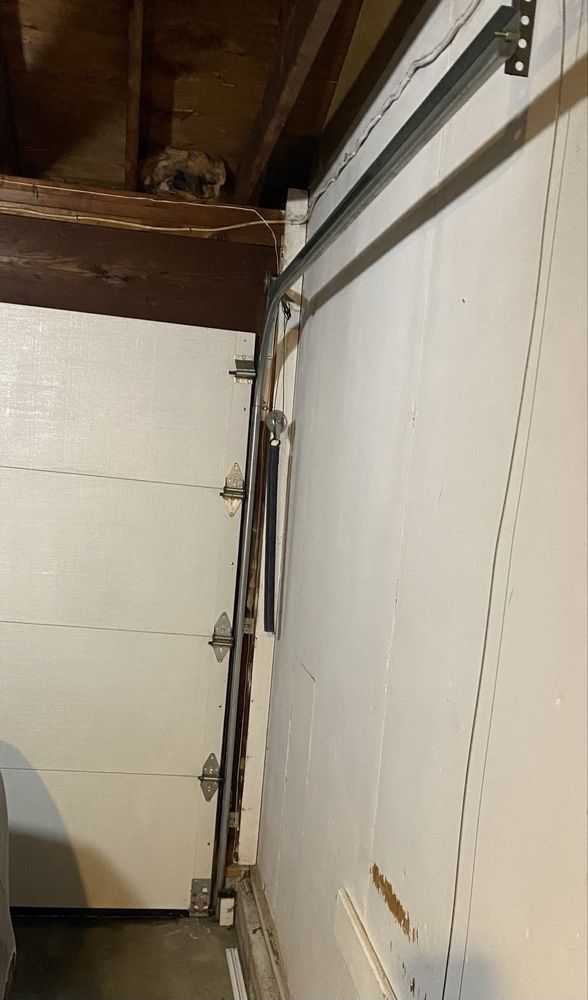 A low-angle view of a white sectional garage door closed against a white wall with metal tracks and hardware attached.