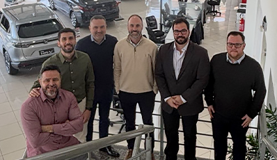 Grupo de sete homens, provavelmente colegas, em pé em uma escada dentro de uma concessionária de automóveis.