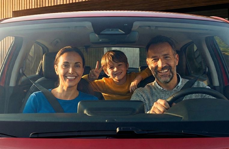 Família sorrindo dentro do Honda HR-V na cor vermelha; criança no banco de trás faz sinal de paz