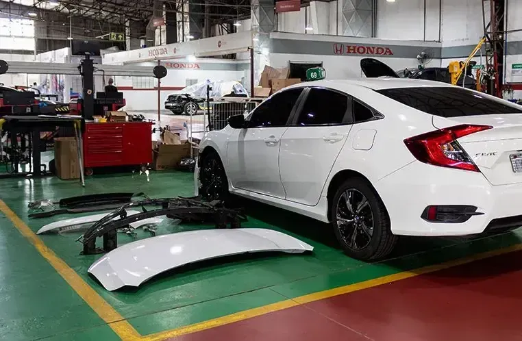 Honda Civic branco em uma oficina mecânica, com peças de carro espalhadas pelo chão.