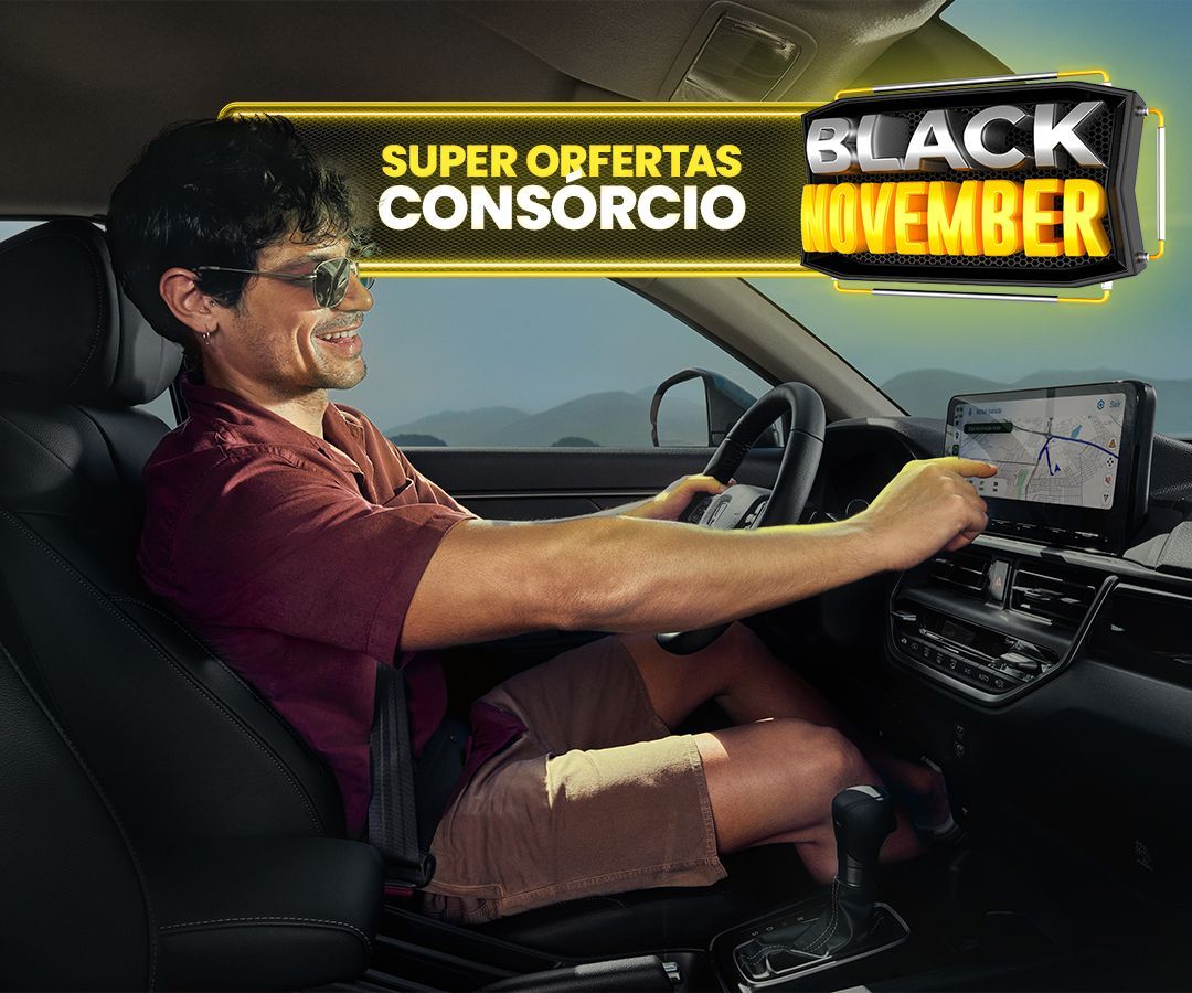 Homem de óculos escuros dentro de um carro, sorrindo para a tela de navegação, em um ambiente externo ensolarado.