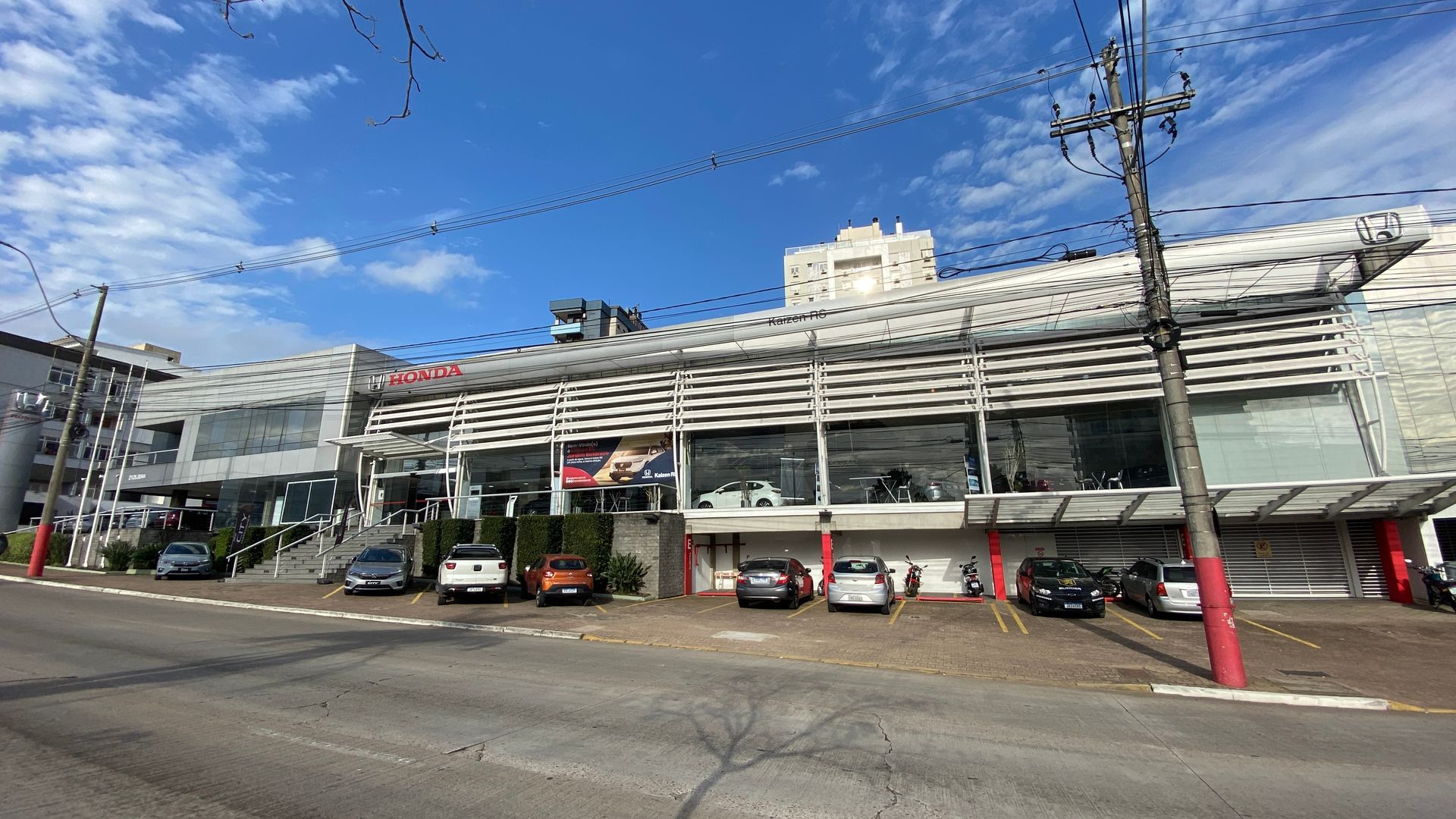 Concessionária de carros em uma rua da cidade com carros estacionados na frente, céu azul.