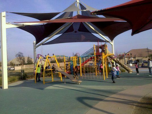 children are playing in a playground under an umbrella
