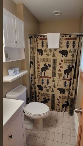 A bathroom with a toilet , sink and shower curtain with moose and bears on it.