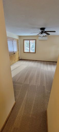 An empty living room with a ceiling fan and two windows.