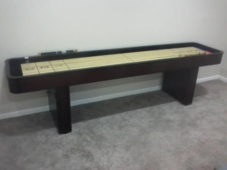 A shuffleboard table is sitting on a carpeted floor in a room.
