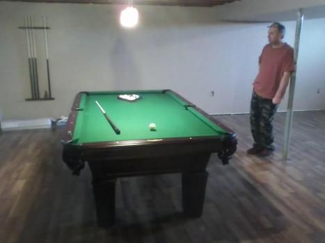 A man is standing next to a pool table in a room.