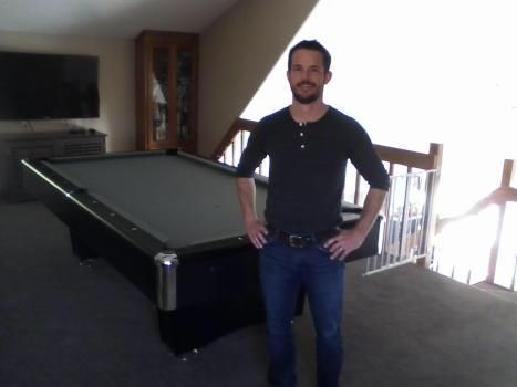 A man standing in front of a pool table with his hands on his hips