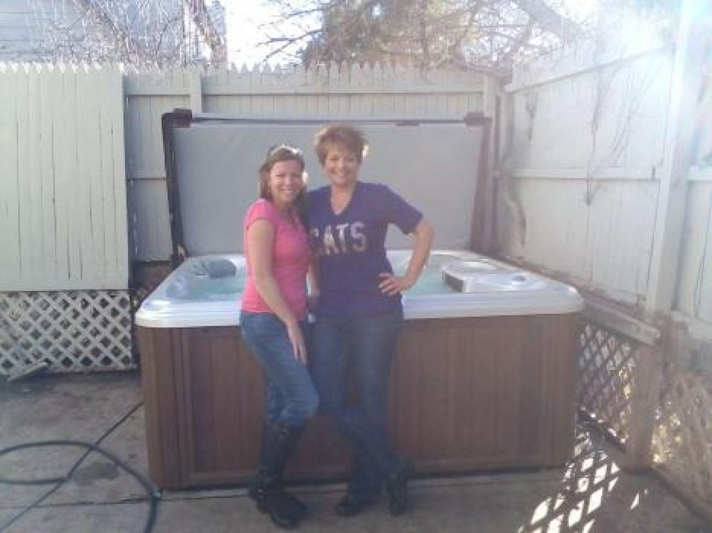 Two women are standing in front of a hot tub . one of the women is wearing a cats shirt.